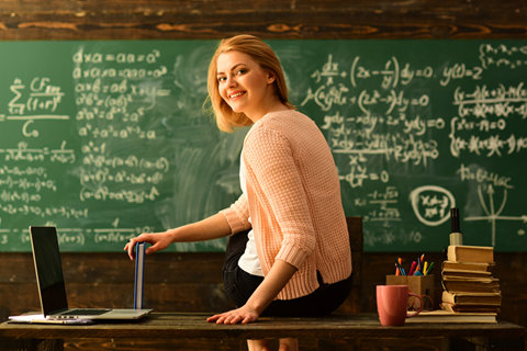 Kvinnelig lærer som sitter på kateteret foran en grønn tavle med ligninger